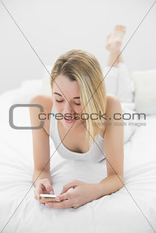 Attractive calm woman texting with her smartphone lying on her bed
