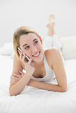 Cute blonde woman phoning with her smartphone lying on her bed