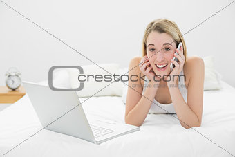 Amused calm woman phoning lying on her bed next to her laptop