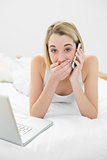 Portrait of attractive surprised woman phoning lying on her bed