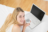 Relaxing blonde woman using her laptop while holding a cup