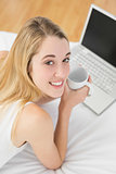 Attractive blonde woman using her notebook holding a cup