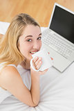Gorgeous young woman drinking of cup lying on her bed
