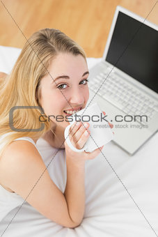 Gorgeous young woman drinking of cup lying on her bed