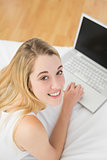 Peaceful blonde woman working with her notebook lying on her bed