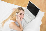 Cute woman phoning while lying on her bed next to her laptop