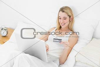 Gorgeous woman home shopping with her notebook lying on her bed