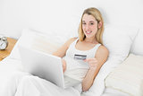 Sweet blonde woman home shopping with her notebook lying on her bed