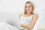 Beautiful young woman lying on her bed using her notebook