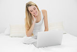 Gleeful cute woman working with her notebook sitting on her bed