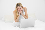 Gleeful young woman working with her laptop sitting on her bed