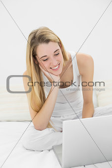 Pretty calm woman using her notebook sitting on her bed