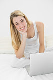 Content woman smiling at camera using her notebook sitting on her bed