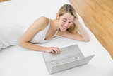 Lovely young woman using her notebook lying on her bed