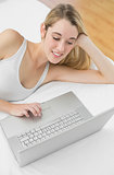 Attractive blonde woman working with her notebook lying on her bed
