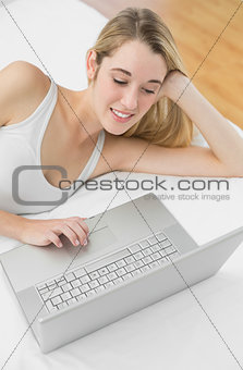 Attractive blonde woman working with her notebook lying on her bed