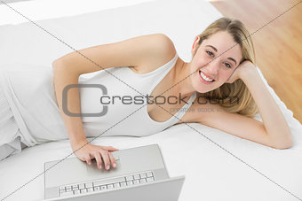Cheerful blonde woman using her notebook smiling at camera