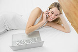 Lovely blonde woman phoning with her smartphone lying on her bed