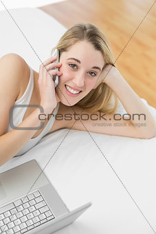 Cute woman phoning with her smartphone lying on her bed