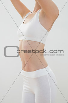 Mid section of slender young woman in sportswear raising her arms