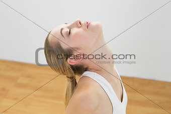 Young toned woman kneeling on floor in sports hall stretching