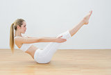 Sporty young woman doing sports exercise sitting on floor