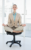 Peaceful chic businesswoman sitting in lotus position on swivel chair