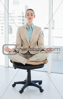Peaceful chic businesswoman sitting in lotus position on swivel chair