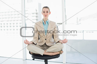 Lovely chic businesswoman sitting in lotus position on her swivel chair
