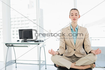 Concentrated calm businesswoman sitting in lotus position on her swivel chair