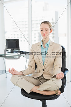 Lovely classy businesswoman meditating in lotus position on her swivel chair