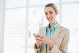 Cute smiling businesswoman holding her smartphone standing in her office