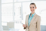 Happy ponytailed businesswoman holding her smartphone smiling at camera