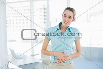 Gorgeous young businesswoman holding her aching belly