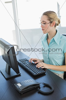 Pretty concentrated businesswoman sitting at her desk working on her computer