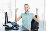 Classy businesswoman cheering sitting at her desk