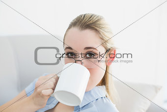 Attractive calm businesswoman sitting on couch drinking from cup