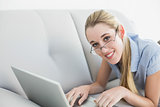 Content calm businesswoman working on her laptop lying on couch