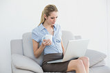 Lovely young businesswoman working on laptop holding a cup