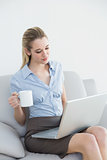 Gorgeous calm businesswoman working on notebook holding a cup