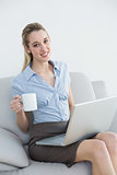 Cheerful ponytailed businesswoman using her notebook holding a cup