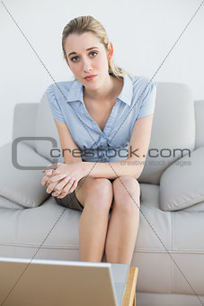 Serious chic businesswoman sitting on couch in front of her laptop