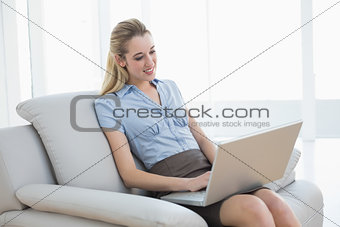 Cheerful classy businesswoman sitting on couch using her notebook