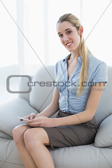 Content pretty businesswoman messaging with her smartphone sitting on couch