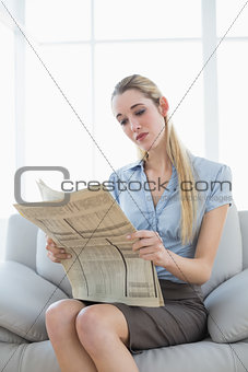 Attractive calm businesswoman sitting on couch while reading newspaper