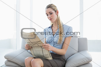 Serious calm businesswoman reading newspaper sitting on couch