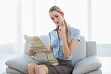 Thoughtful lovely businesswoman reading newspaper while sitting on couch