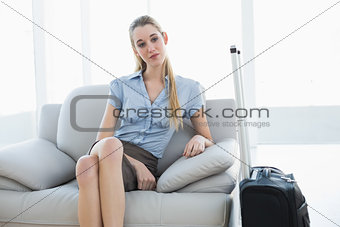 Day dreaming chic businesswoman sitting on couch next to her suitcase