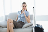 Chic businesswoman posing sitting on couch nest to her suitcase