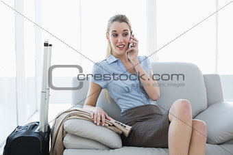Pretty blonde businesswoman phoning with her smartphone sitting on couch